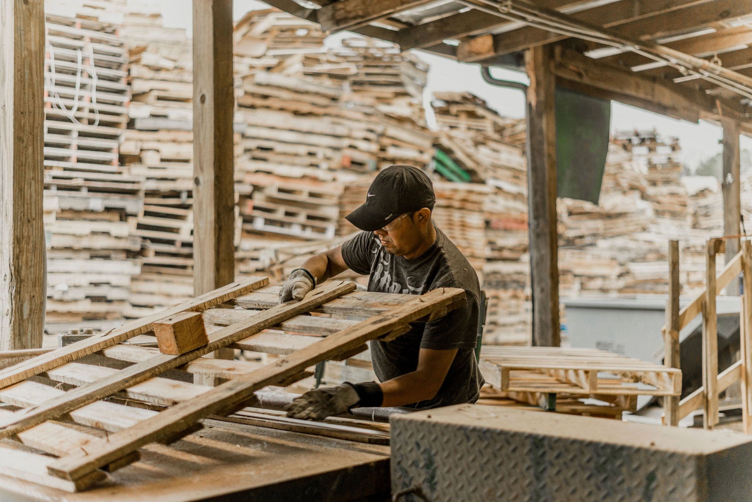 A J.C. Pallet team member working in the pallet yard with stacked pallets in the background