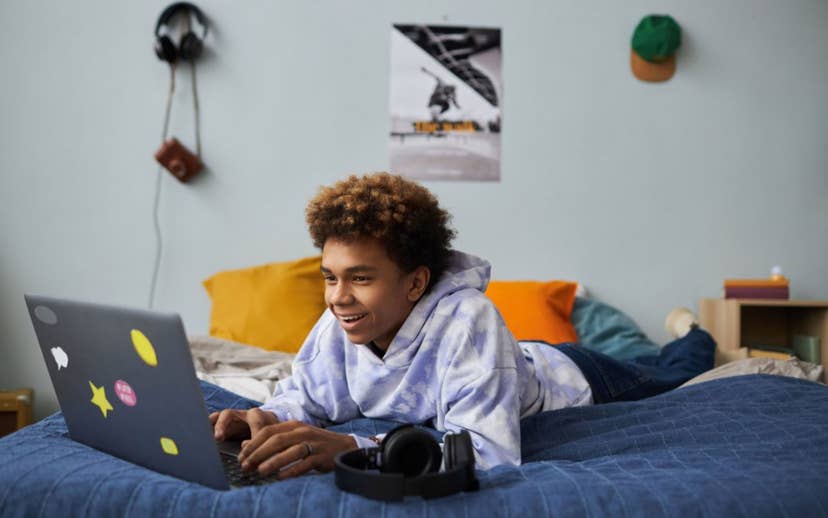 teen boy on laying on bed with laptop