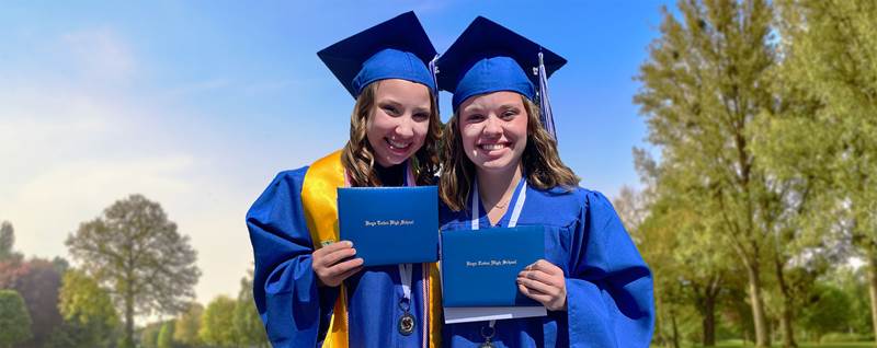Two teen girls smiling in their blue graduation caps and gowns.