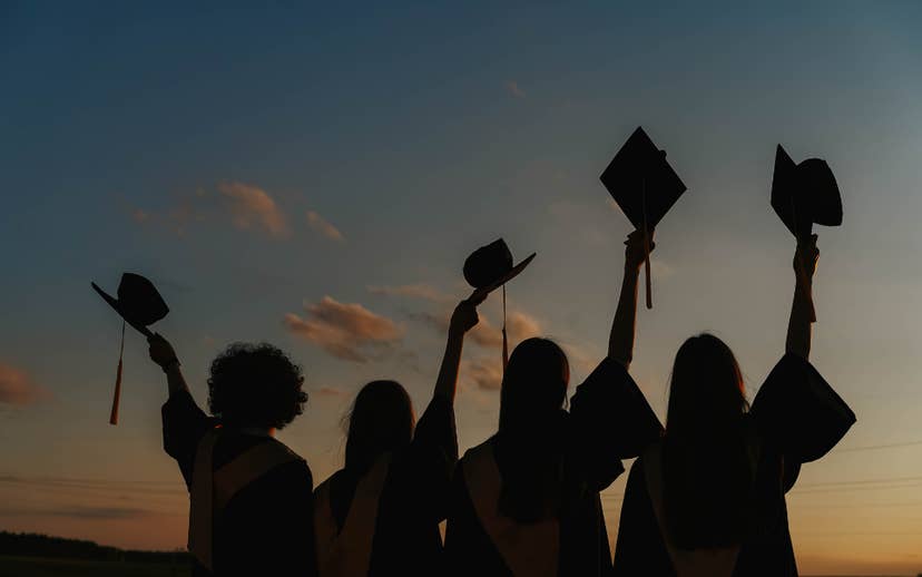 4 youth silhouettes holding graduation caps up in air