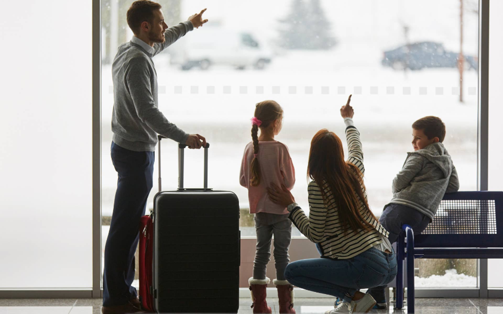 Mom and Dad with suitcase looking out window with 2 young children
