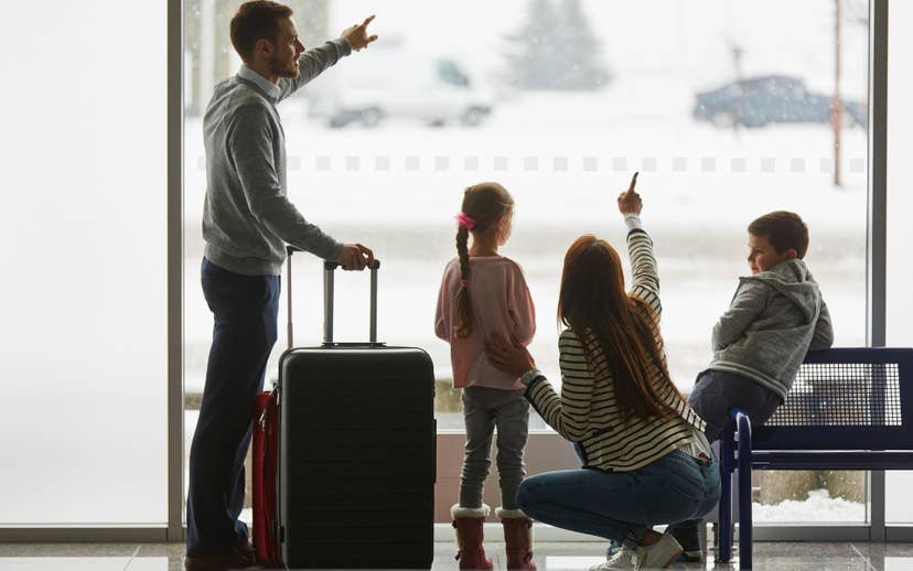 Mom and Dad with suitcase looking out window with 2 young children