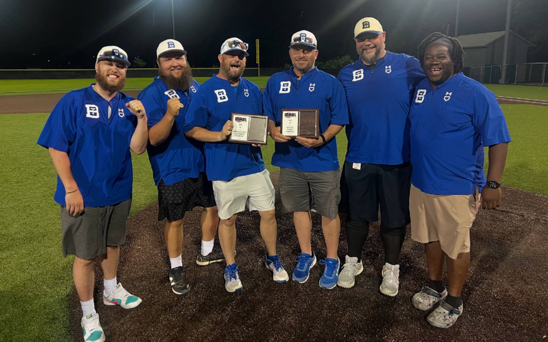 Group of men gathered around on a baseball field wearing matching blue shirts