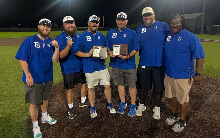 Group of men gathered around on a baseball field wearing matching blue shirts