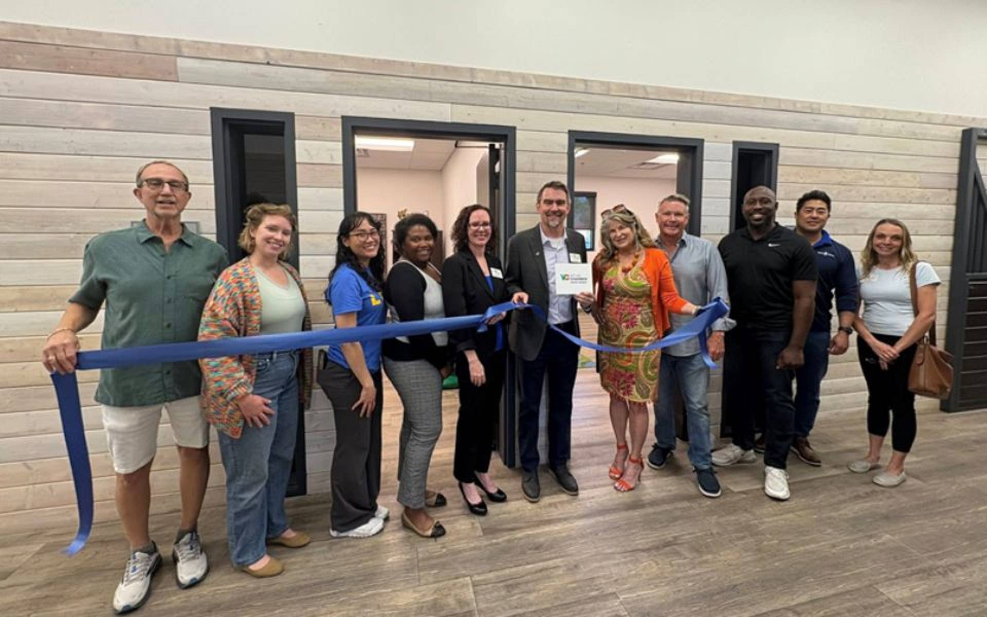 Group of men and woman standing behind a ribbon cutting