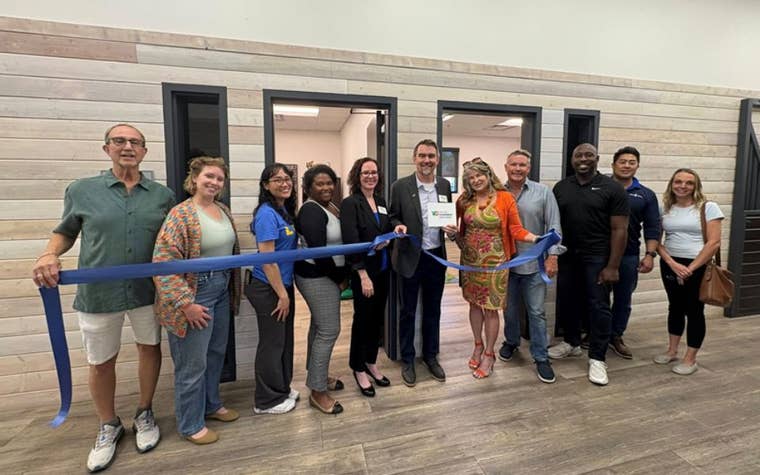 Group of men and woman standing behind a ribbon cutting