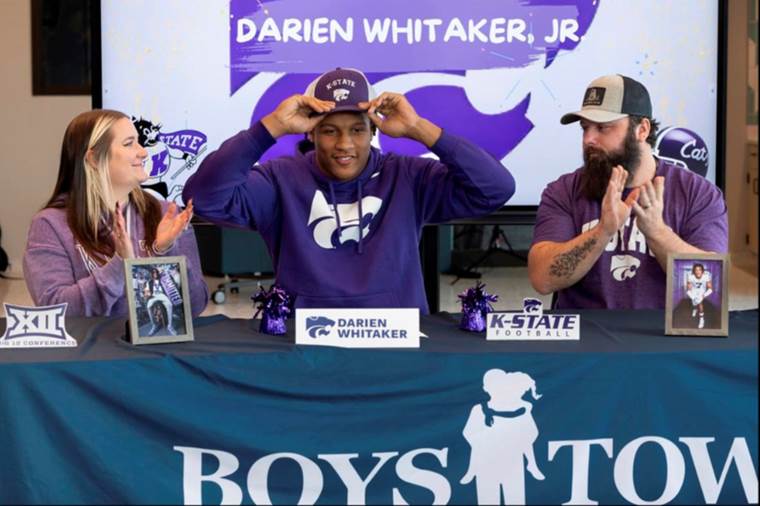 High school student putting on the hat of the school he has chosen to go to college on a football scholarship 