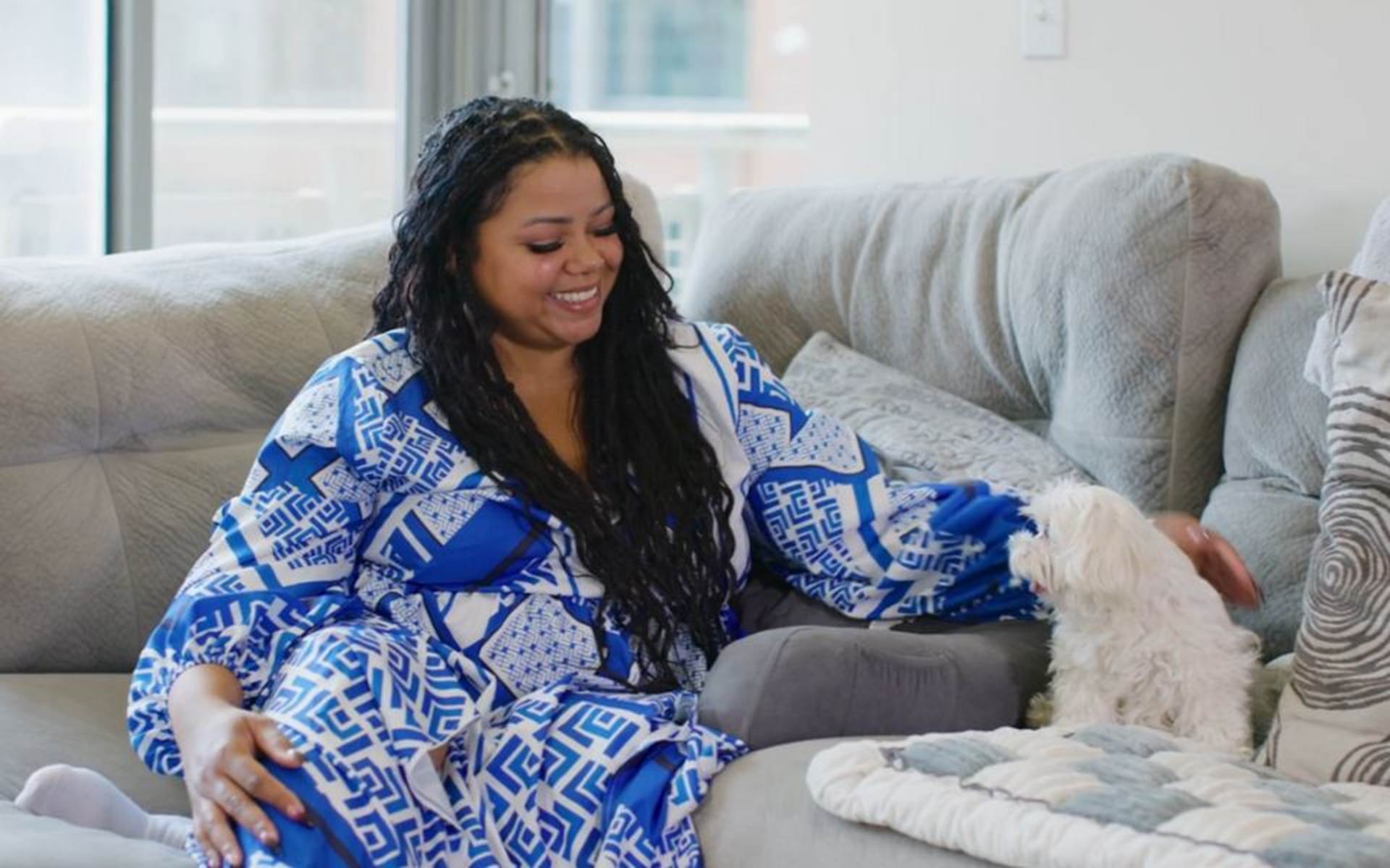 woman sitting on a couch petting a small dog 