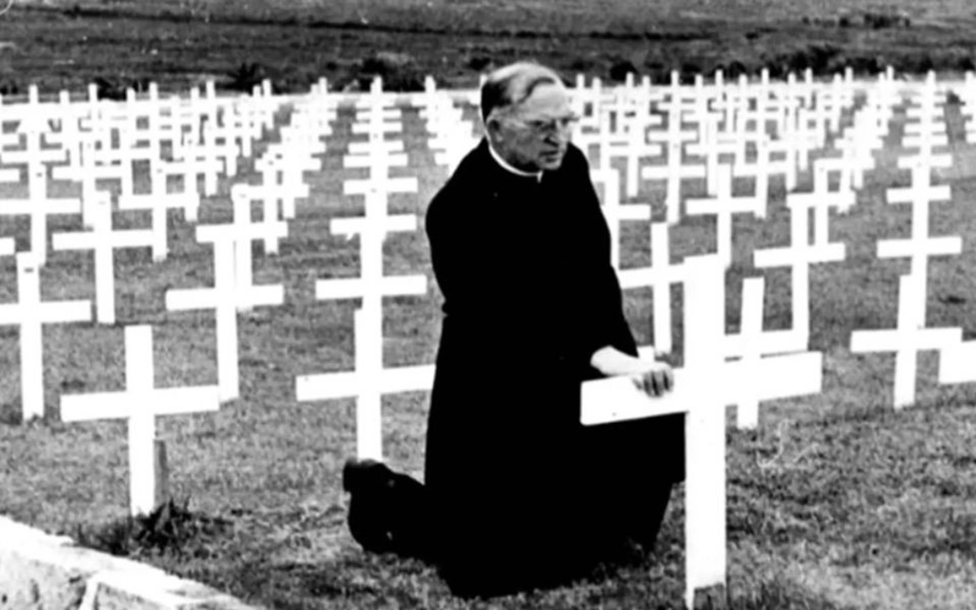 Father Flangan kneeling down to show respect at a gravestone marked with a cross