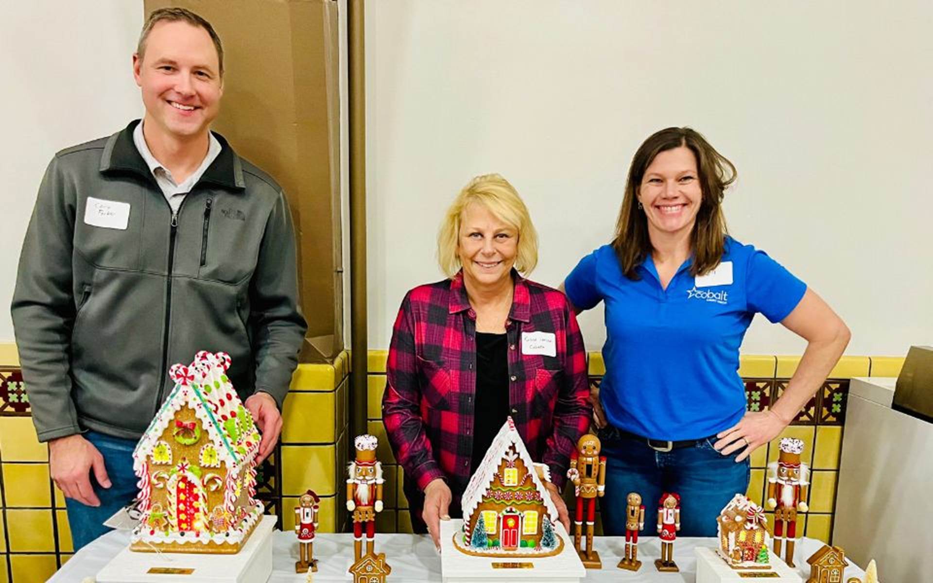 man and two women standing by a table with different gingerbread houses