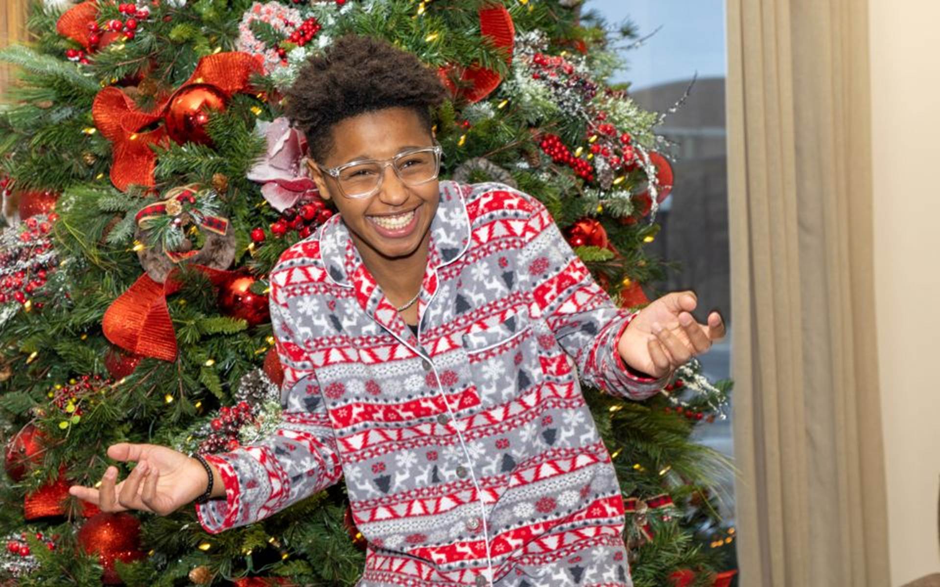 Boy in Christmas pajamas standing in front of a decorated Christmas tree 