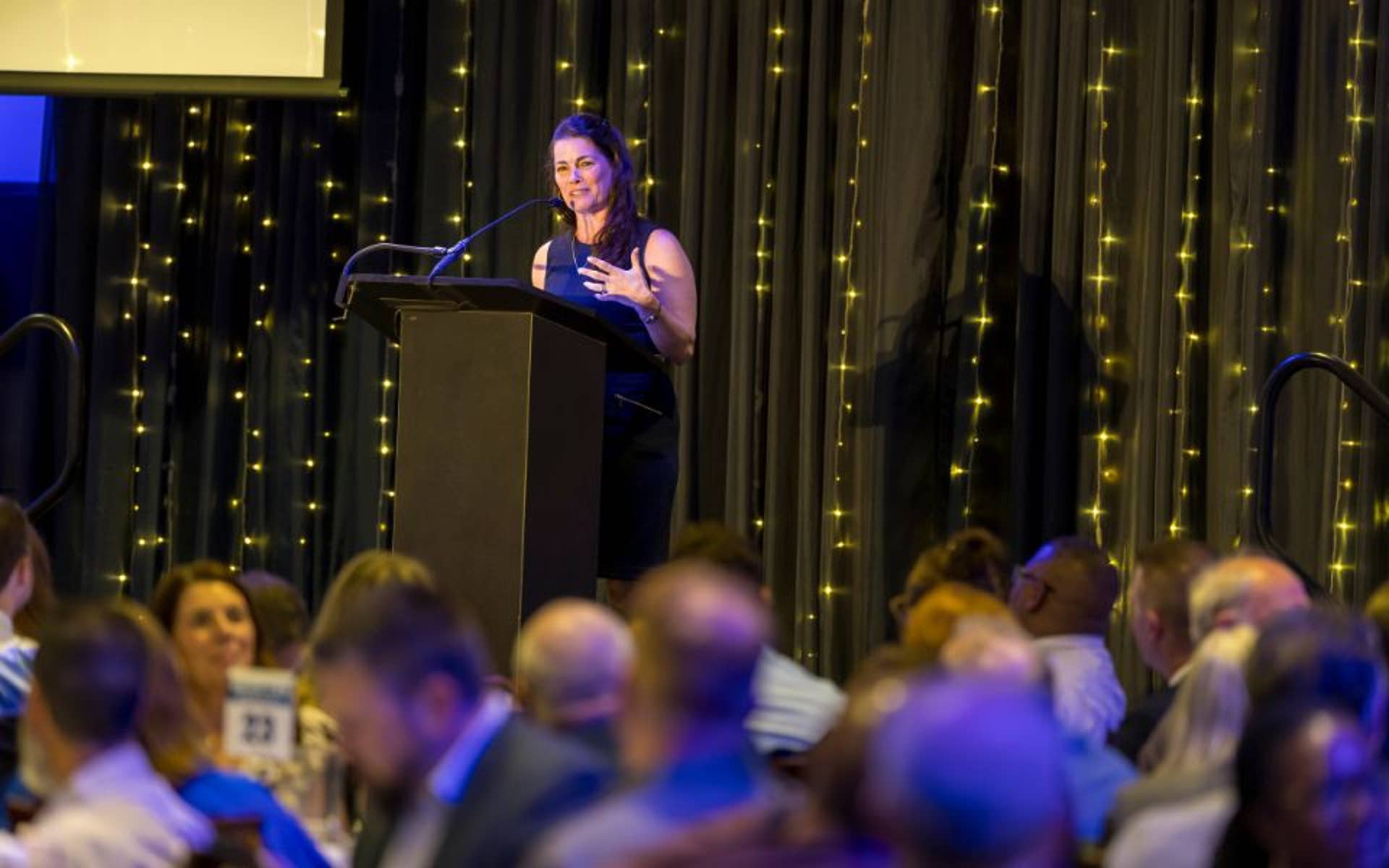 Woman speaking at a podium in front of a large audience 