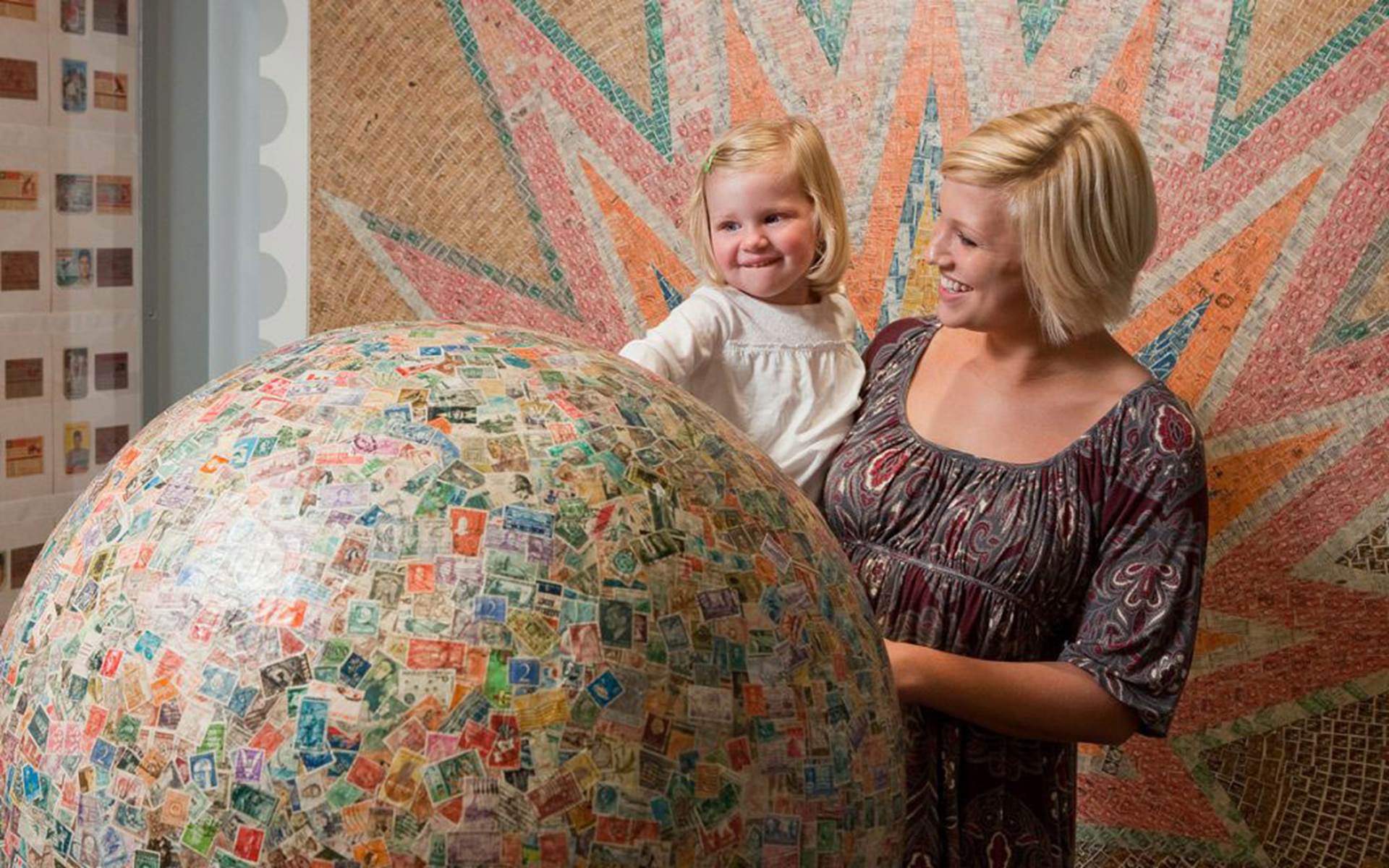 Mom holding daughter while looking at the worlds largest stamp ball