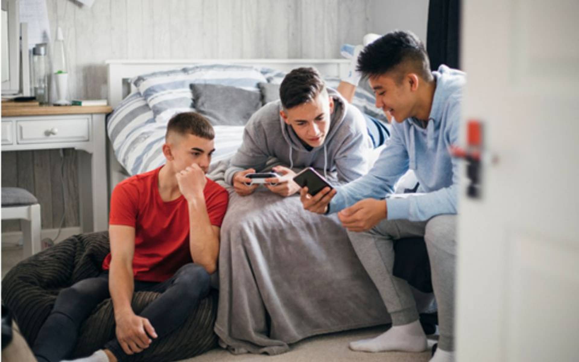 Three teenage boys hanging out in a bedroom all looking at their phones
