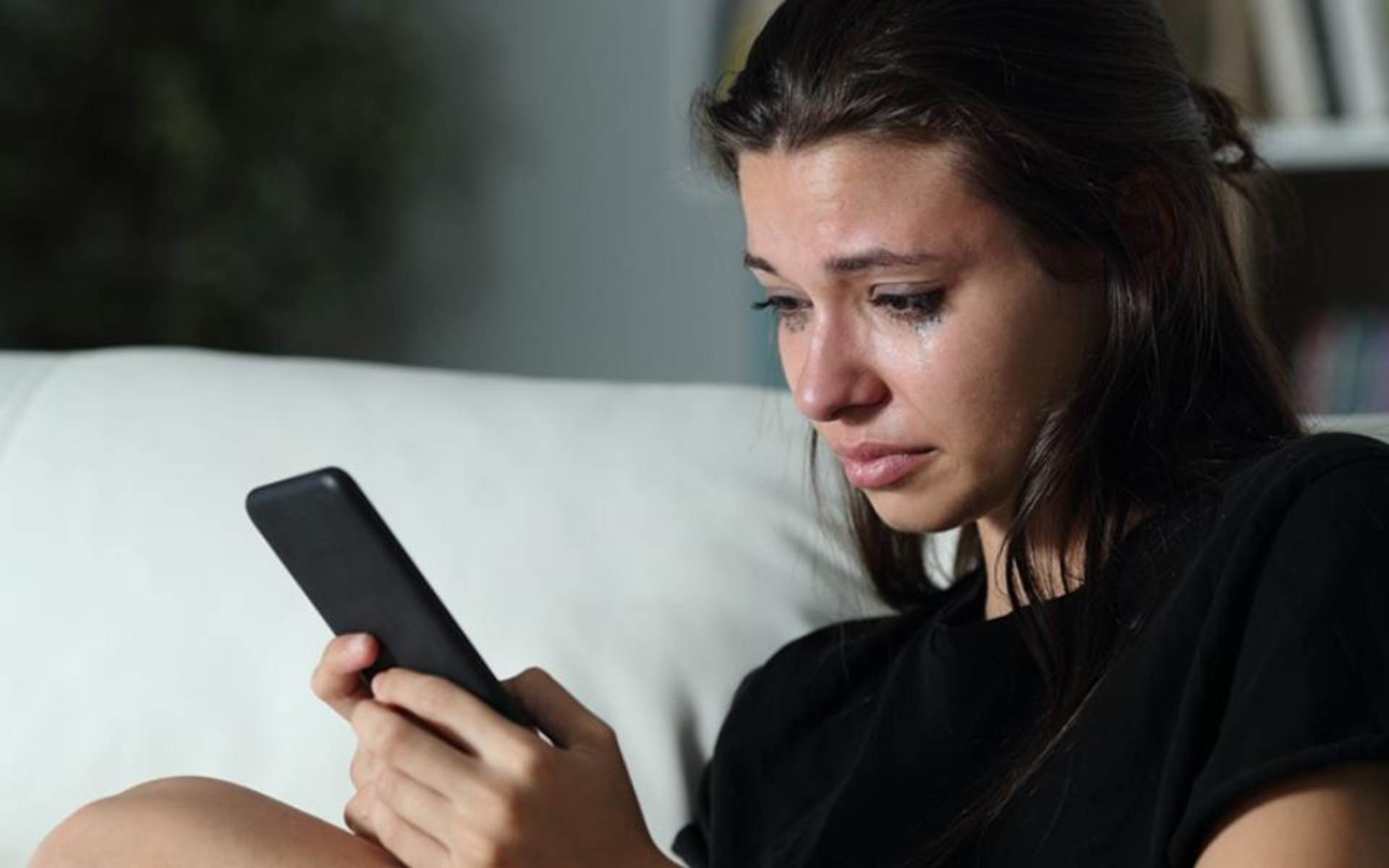 Teenage girl crying while staring at her smart phone