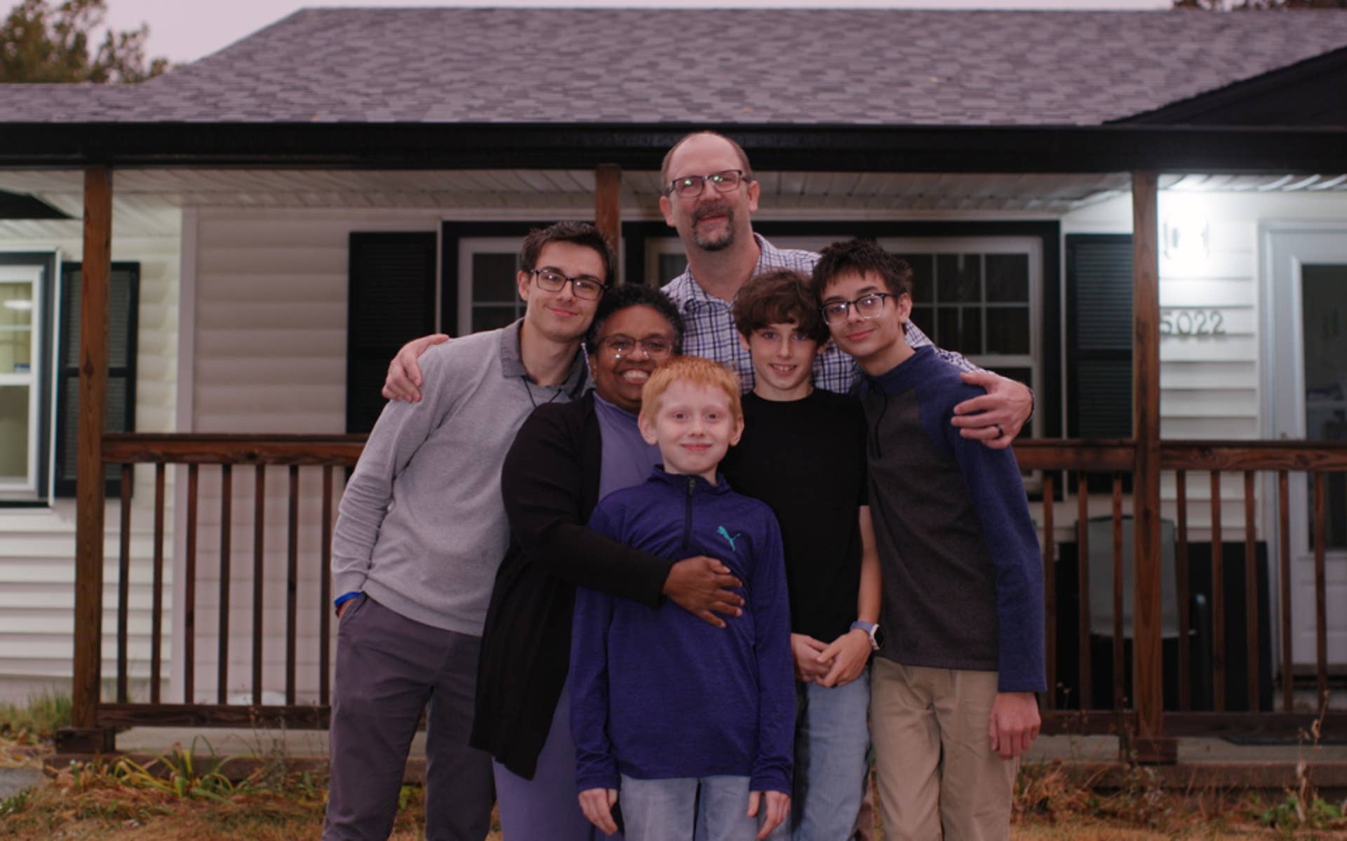 A family standing outside their home all in a group hug