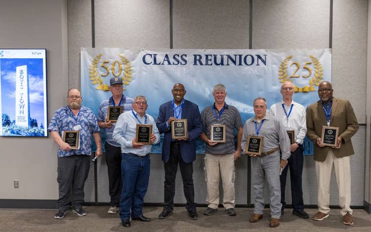 a group of men holding awards in front of a class reunion sign on the wall 
