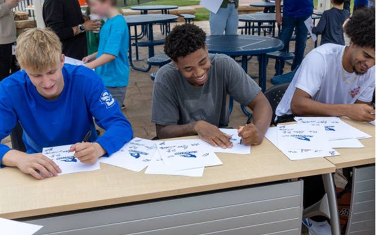 three young men signing papers sitting down