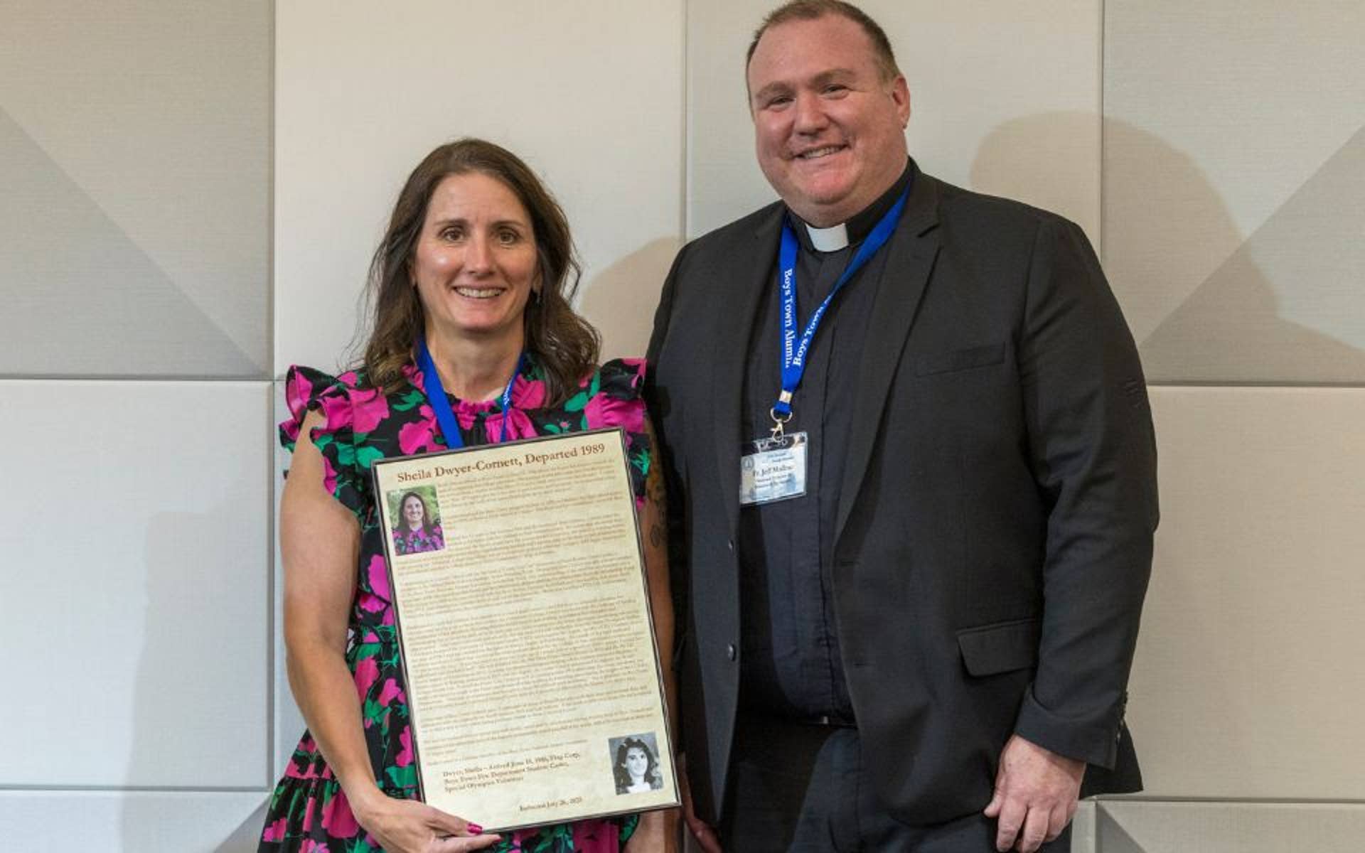 Sheila Dwyer-Cornett standing Father Mollner, holding a Hall of Fame induction plaque.