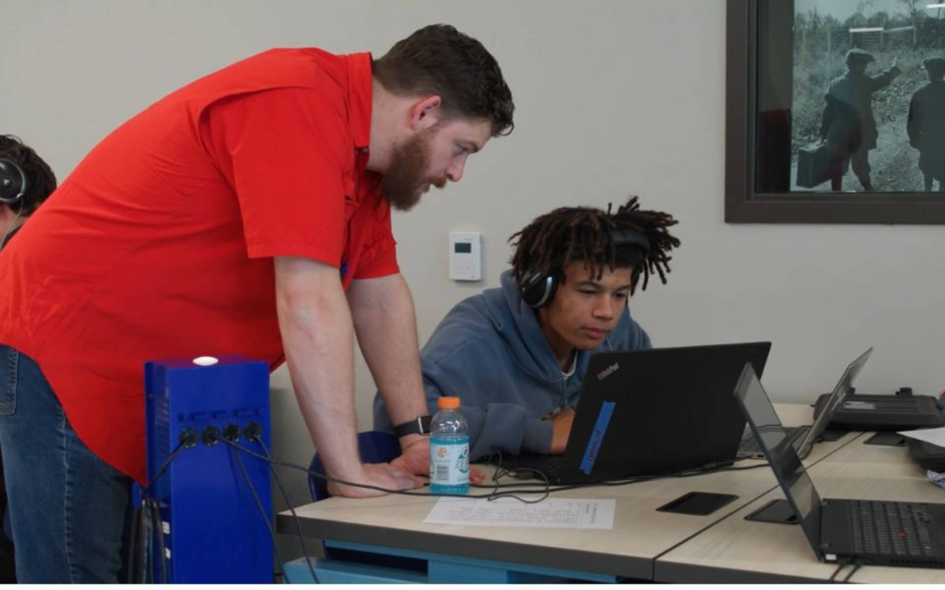 Adult man looking over work as a teenager types on laptop