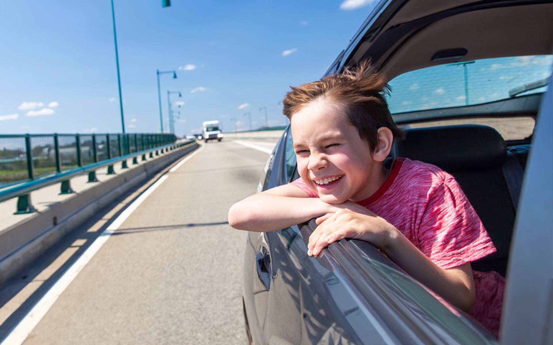 young boy hanging head out of the window of a moving car