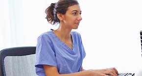 A women wearing scrubs typing on a computer