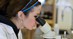 Woman in a lab coat looking into a microscope 