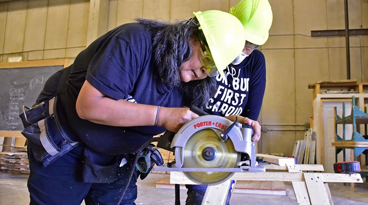 Aboriginal woman using saw in construction lab