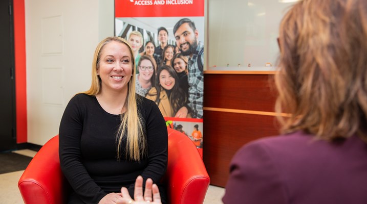 Erin Plourde sitting in a chair and speaking with another person 