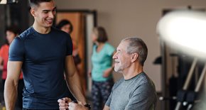 Young man training an older man in the gym