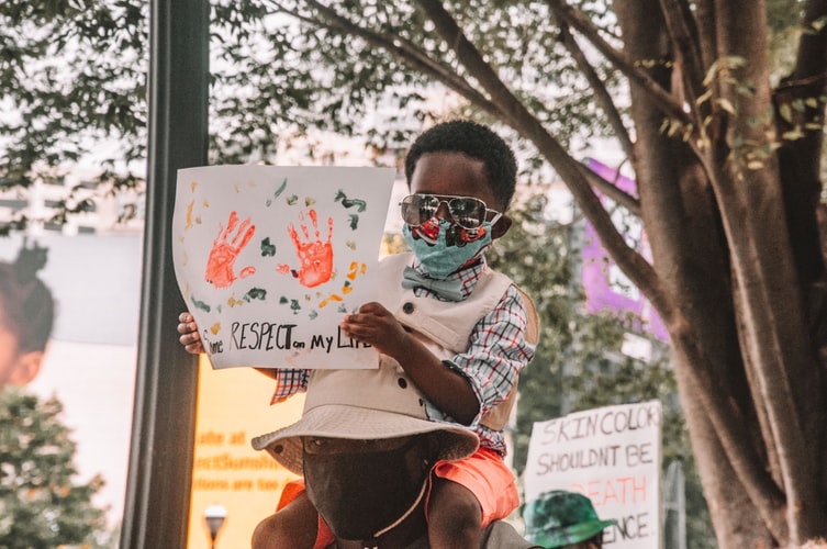 A black child holding a sign on the top of his dad's shoulders