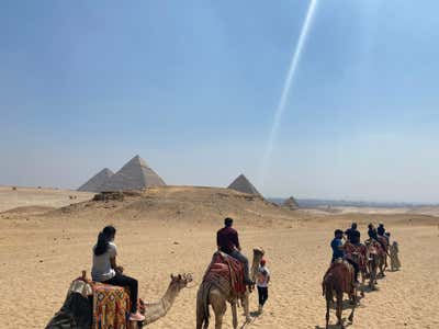 Riding camels toward the pyramids at Giza with beams of light hitting the tips