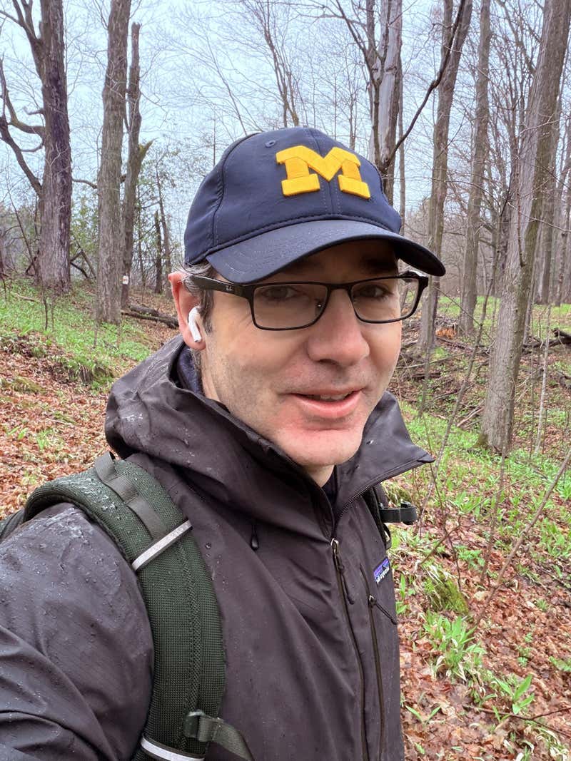Selfie on the trail in a Michigan ball cap and Patagonia jacket, hair damp from rain