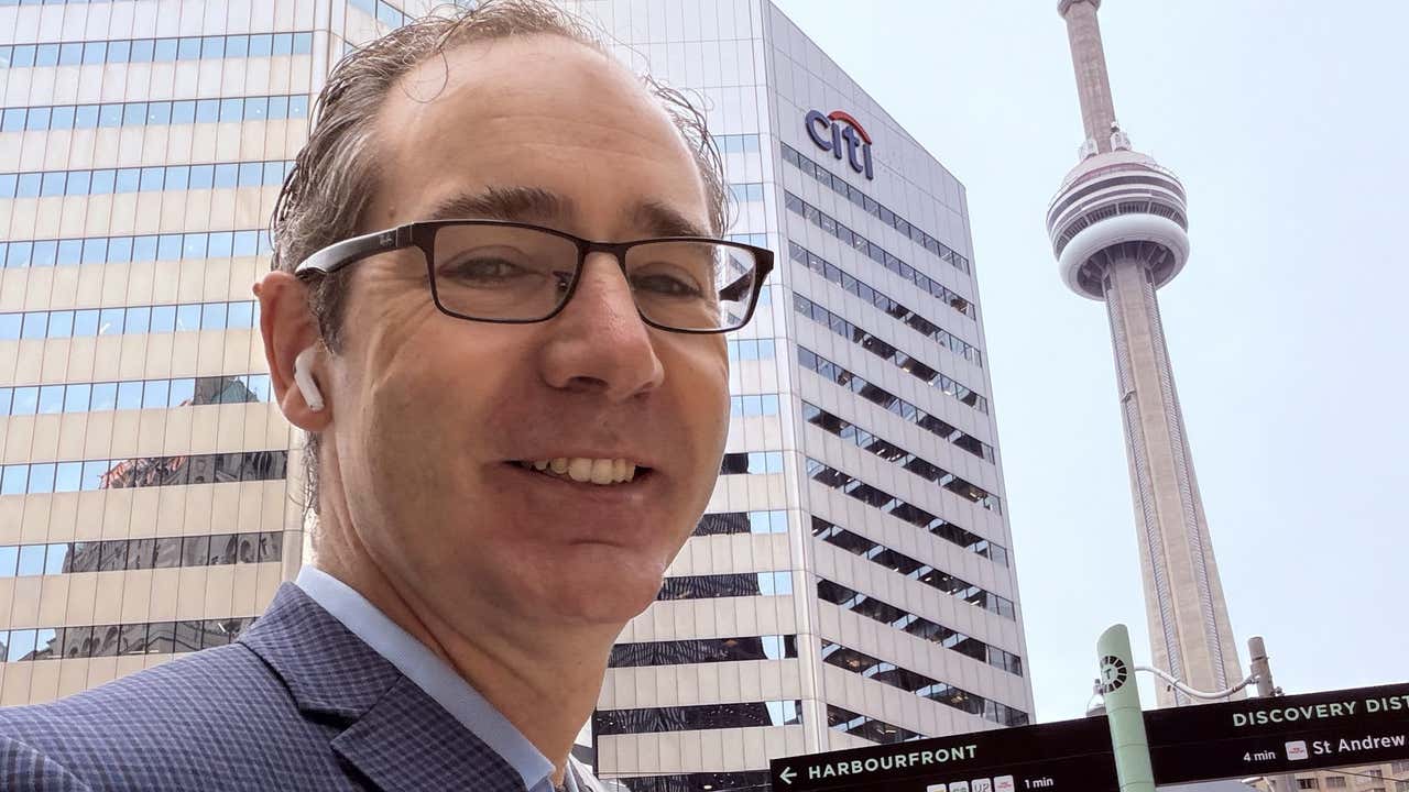 Joel smiling in downtown Toronto with the Citi building and the CN Tower behind him