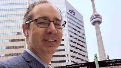 Joel smiling in downtown Toronto with the Citi building and the CN Tower behind him