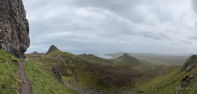 The path hugging the cliff on the left, then the switchbacks dropping down into the green with the sea beyond