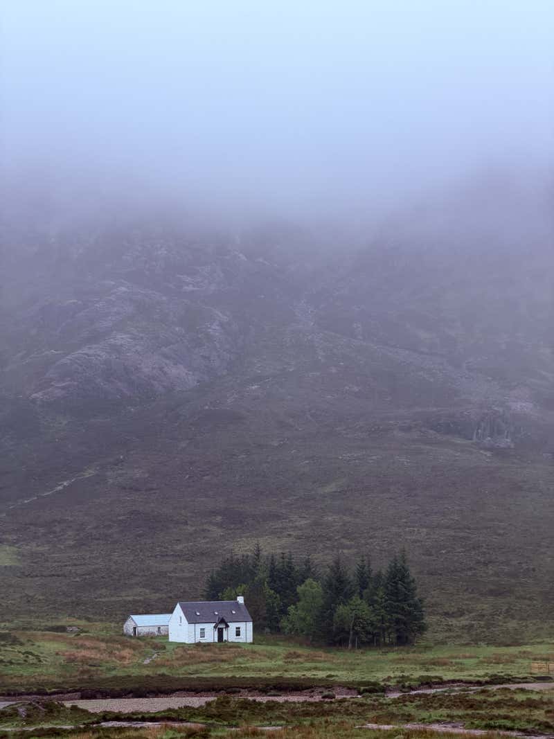 A lone white cottage tucked into the glen, the mountains lost in cloud above it