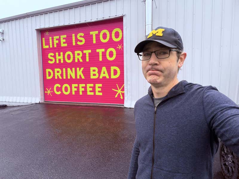 Selfie outside Silver Scooter Roasters next to a pink garage door painted with the words 'Life is too short to drink bad coffee'