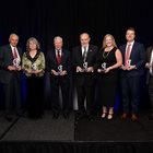 Seven KCU Alumni Award Winners stand together, each holding a trophy in the shape of the caduceus. 