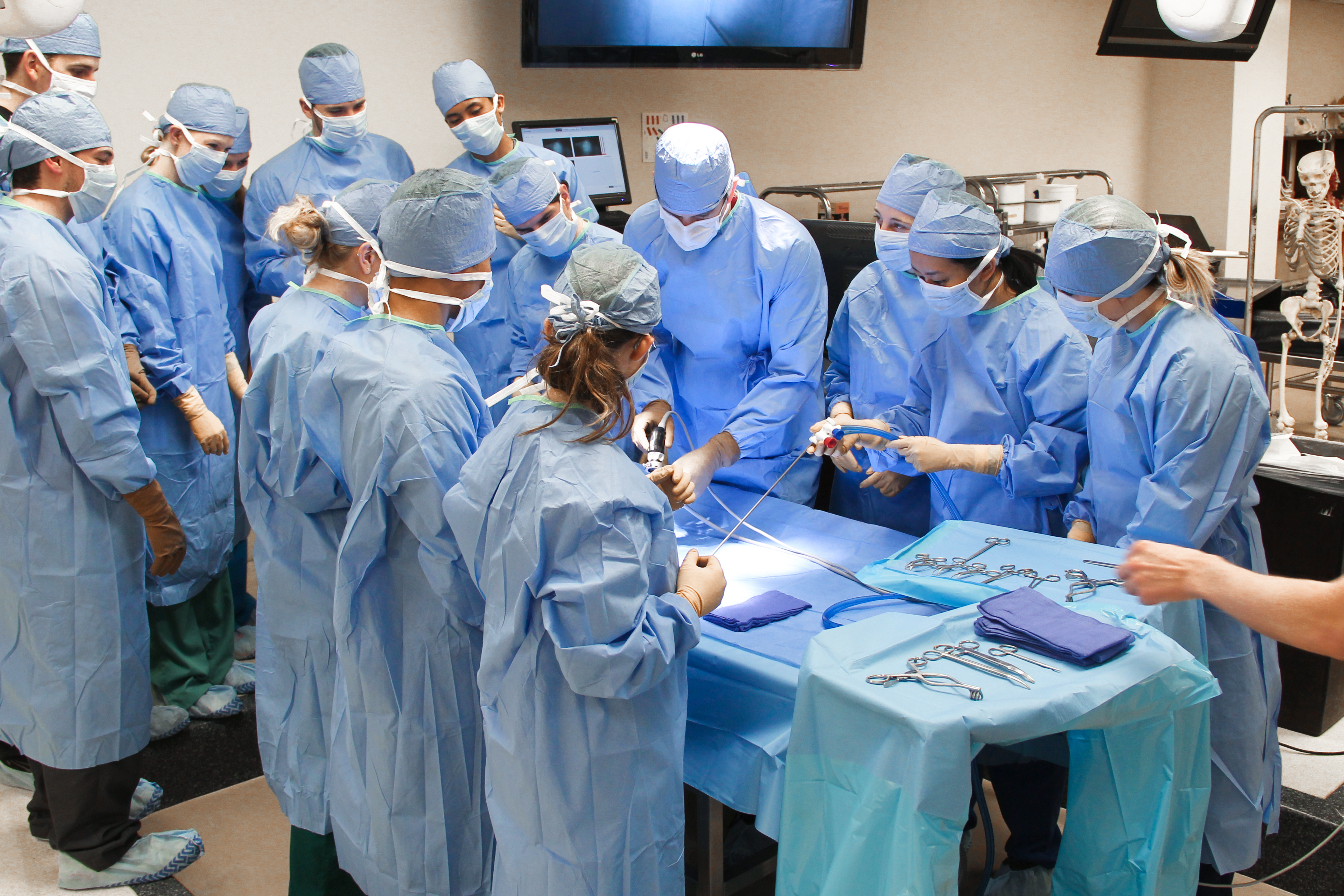 Students learn together around surgical table while in surgical gowns. 