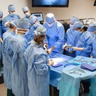 Students learn together around surgical table while in surgical gowns. 