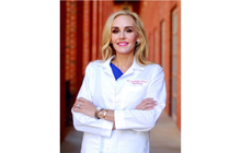 Katherine Pannel stands in front of red brick with arms crossed in her white coat. 