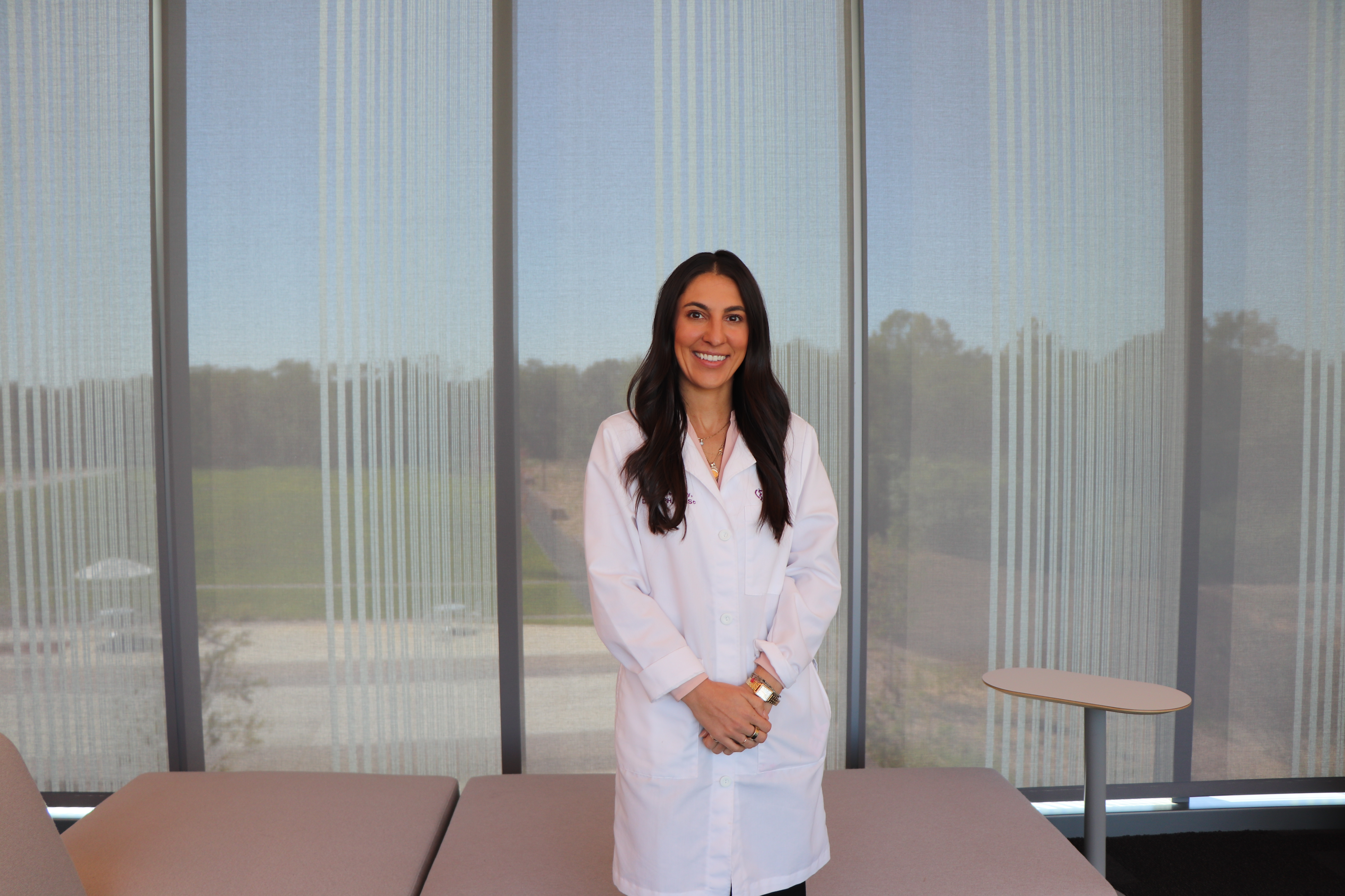 Dr. Kennedy stands in front of shaded window in her white coat. 