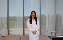 Dr. Kennedy stands in front of shaded window in her white coat. 