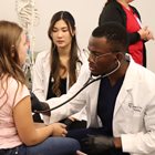 Student doctor in white coat checks young child's heart with a stethoscope. 