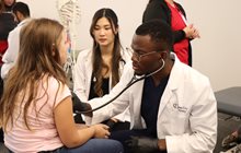 Student doctor in white coat checks young child's heart with a stethoscope. 