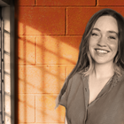  Kari Jo West poses in front of orange cinderblock and metal bars. 