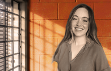  Kari Jo West poses in front of orange cinderblock and metal bars. 