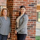 Drs. Jennifer Fugate and Nicki Zieber smile together in front of brick wall. 