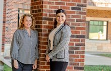 Drs. Jennifer Fugate and Nicki Zieber smile together in front of brick wall. 